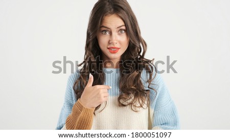 Beautiful brunette girl in sweater pointing fingers on herself and amazedly looking in camera isolated