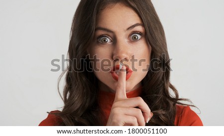 Portrait of excited brunette girl showing silence gesture over white background. Keep secret expression