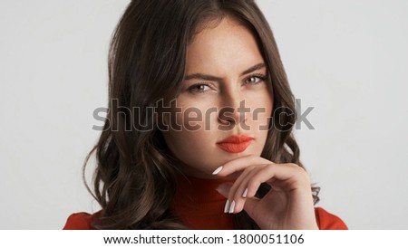 Portrait of attractive tricky brunette girl thoughtfully looking in camera over white background