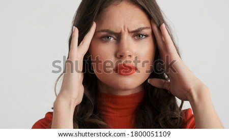 Portrait of angry brunette girl sadly showing headache on camera over white background