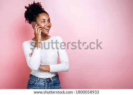 Photo of happy young woman standing isolated over pink background. Looking aside talking by phone.