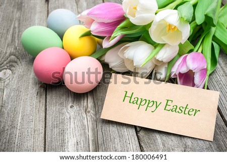 Easter eggs and tulips with a tag on wooden background