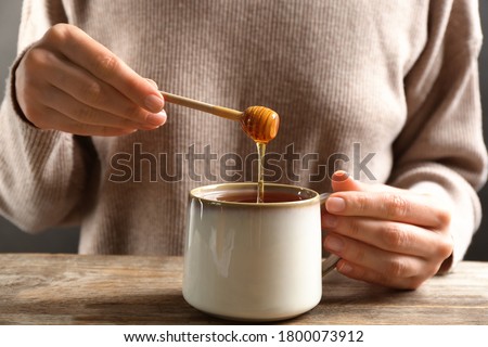 Woman putting honey into tea at wooden table, closeup