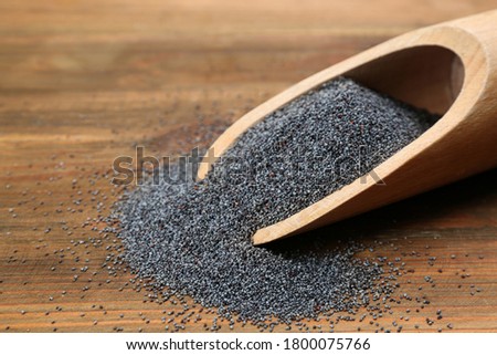 Poppy seeds in scoop on wooden table, closeup
