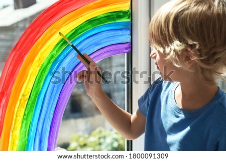 Little boy drawing rainbow on window indoors. Stay at home concept