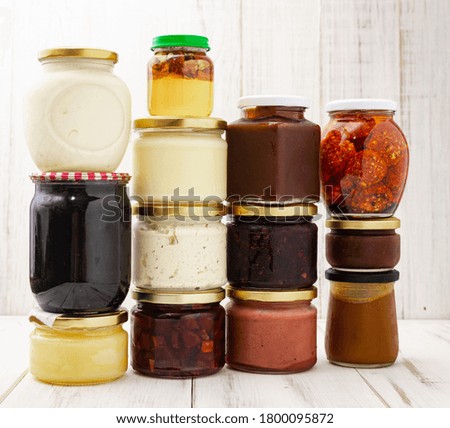 Various jars with canned vegetables, oils on a light wooden background.