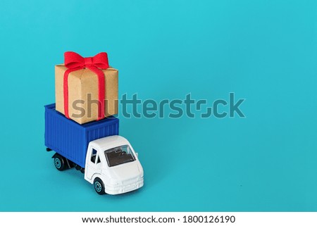 Car delivering gift box on blue background. Cargo transportation, delivery service. Transport company. Infrastructure and logistics. Unloading cardboard box. Place for text