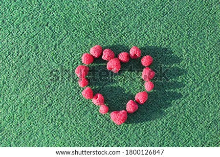 Raspberries fruits in shape of a heart. Green background. Love