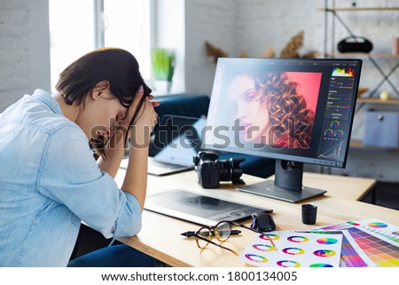 Portrait of tired graphic designer working overtime in office. Stressed worker have eye strain symptoms. Retoucher workplace in photo studio. Burnout and overwork concept. Creative agency.