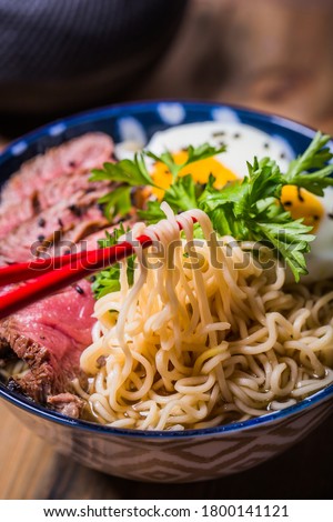 Ramen Soup with Wagyu Beef Filet in Bowl on wooden table. Beef ramen served Asian style. Raw egg cooks in steaming hot savory broth.