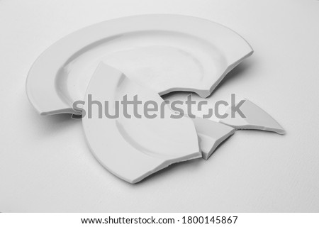 fragments of a broken plate on a light background, black and white photo. The concept of breaking up relations, divorce, destruction Royalty-Free Stock Photo #1800145867