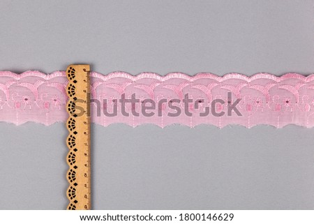 straight strip of pink cotton ribbon with embroidery and wooden ruler on gray background. National pattern for sewing. pattern and interweaving threads. texture for websites. Space for text.