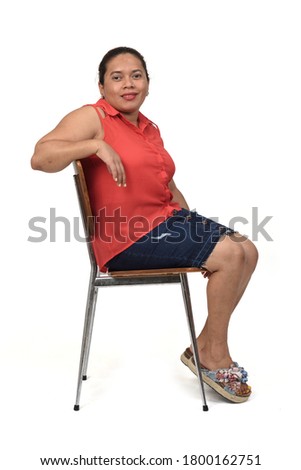 portrait of a woman sitting on a chair with the body in profile and looking at the camera on white background,