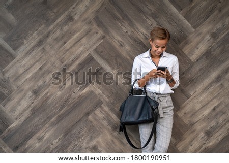 Smiling business woman using cell phone over brown wooden wall stock photo