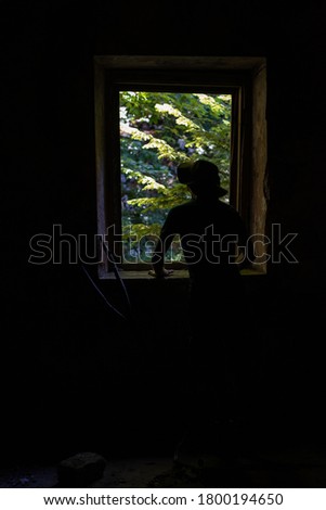 Man looking outside of a window, silhouette, dark room