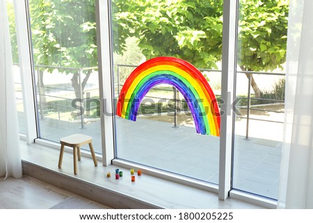 Painting of rainbow on window and paints indoors. Stay at home concept