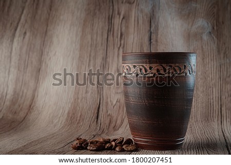 Freshly brewed hot coffee in a tall red clay cup, coffee beans scattered nearby