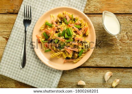 a plate of pasta with ham and mushrooms in a creamy sauce on the table with a fork on a napkin.