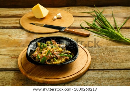 Black plate with pasta with ham and mushrooms in a creamy sauce on the table with a fork in the background.