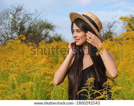 portrait of a beautiful young woman with long dark hair, in a straw hat, in a blooming garden.