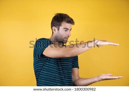 handsome man over isolated yellow background gesturing with hands showing big and large size sign, measure symbol
