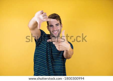 Young handsome man over yellow isolated background doing frame using hands palms and fingers, camera perspective