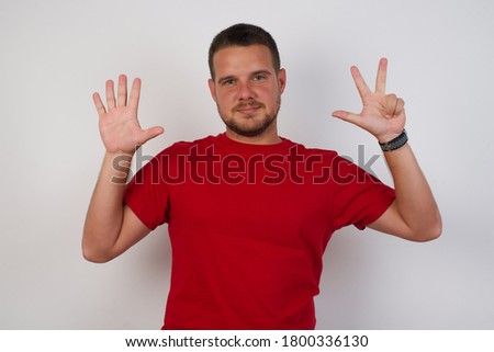 Young handsome man wearing casual red t-shirt over white isolated background showing and pointing up with fingers number eight while smiling confident and happy.