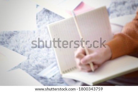 Blurred picture of  hand holding  pencil to write a memory in every story in her notebook.