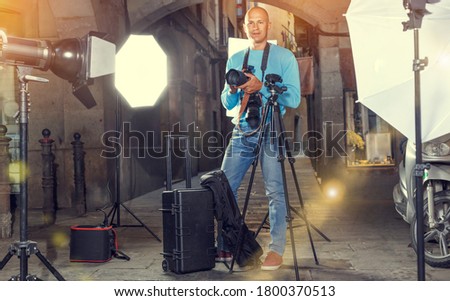 Portrait of male photographer standing with camera among professional photo equipment at old city street