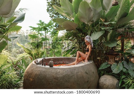 Young woman in whitel towel on her had takng floral bath in tropical jungle. Concept of luxurious spa, aromatherapy Royalty-Free Stock Photo #1800400690