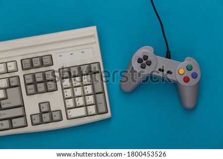 Old keyboard and old-fashioned gamepad on a blue background. Retro gaming. 80s. Top view. Flat lay