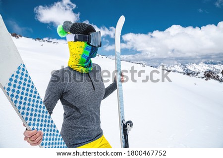 Portrait of a women skier without jacket in a ski mask with her face closed on a sunny day against the backdrop of snow-capped Caucasian mountains and clouds
