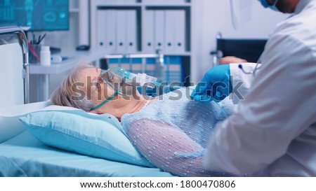 Medical stuff adjusting oxygen mask on senior woman who lies in hospital bed fighting with coronavirus covid-19 symptoms. Medicine medical healthcare system epidemic lungs infection treatment Royalty-Free Stock Photo #1800470806