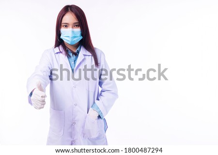 Friendly young woman doctor wear coat uniform and medical face mask holding thumb up while standing over isolate white background. Healthy care and insurance concept.