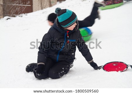 A boy rides from a snow slide on a red cardboard. Fun games in the snow.  Snowy winter in Russia.