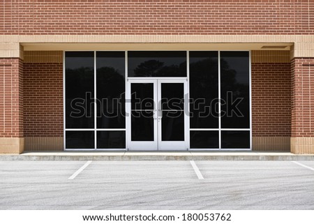 A new unoccupied generic store front, business or professional office space in a contemporary strip mall. Red brick with dark tinted windows in brushed aluminum frames and a double door. Royalty-Free Stock Photo #180053762