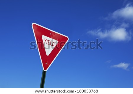 Brightly colored red and white yield sign against dark blue sky with clouds. Some clouds are reflected in the yield sign. Plenty of space for your copy. Photographed on a public highway.