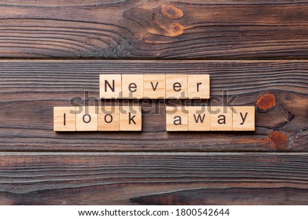 Never look away word written on wood block. Never look away text on wooden table for your desing, concept.
