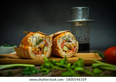 Snack at break time. Famous Vietnamese food is Banh mi thit and black coffee, popular street food from bread stuffed with raw material: pork, ham, pate, egg and fresh herbs.Typical Vietnamese sandwich Royalty-Free Stock Photo #1800546109