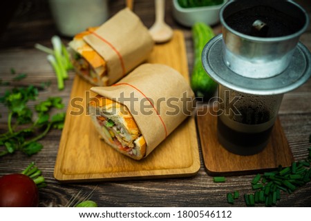 Snack at break time. Famous Vietnamese food is Banh mi thit and black coffee, popular street food from bread stuffed with raw material: pork, ham, pate, egg and fresh herbs.Typical Vietnamese sandwich Royalty-Free Stock Photo #1800546112
