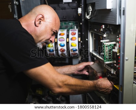 Mature man repairing slot machine Royalty-Free Stock Photo #1800558124