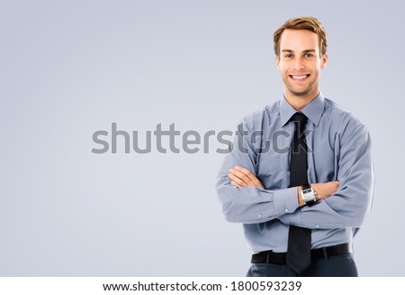 Portrait of happy smiling businessman, standing in crossed arm pose, against grey color background with copy space for some text. Business success concept picture. Man in confident clothing at studio.