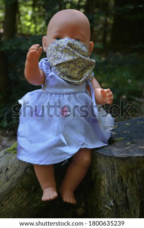 A doll in a purple dress wearing a mask. The picture was taken in the forest.