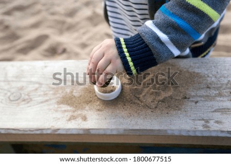 Hand of a little boy in a striped sweater and t-shirt sprinkles a plastic cover with sand
