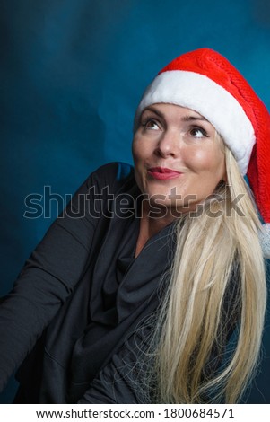 Blonde, long hair women in a Santa hat, smiling, photo in the studio, black background, Happy new year concept