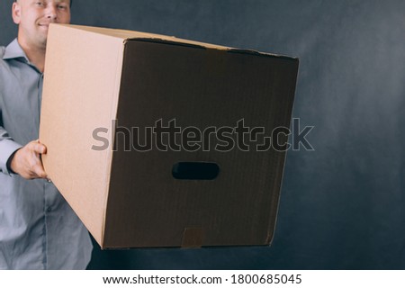 Guy with a cardboard box in his hands. Delivery service concept on dark background