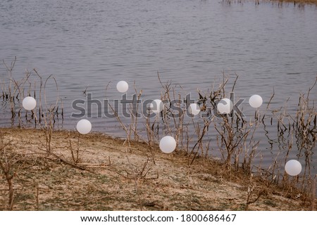 The tied white balloons are near the river or the shore on the breezing day for background.