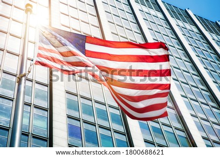 Floating American flag in front of office building with a strong light flare. Royalty-Free Stock Photo #1800688621