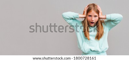 Studio shot of young preteen blonde girl, standing against gray background