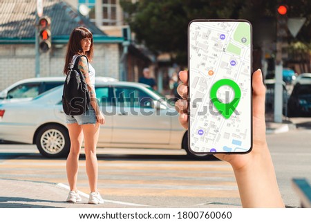 A hand holds a smartphone with an online map app and a marked destination. In the background, a woman stands at a pedestrian crossing. The concept of online navigation and modern technologies